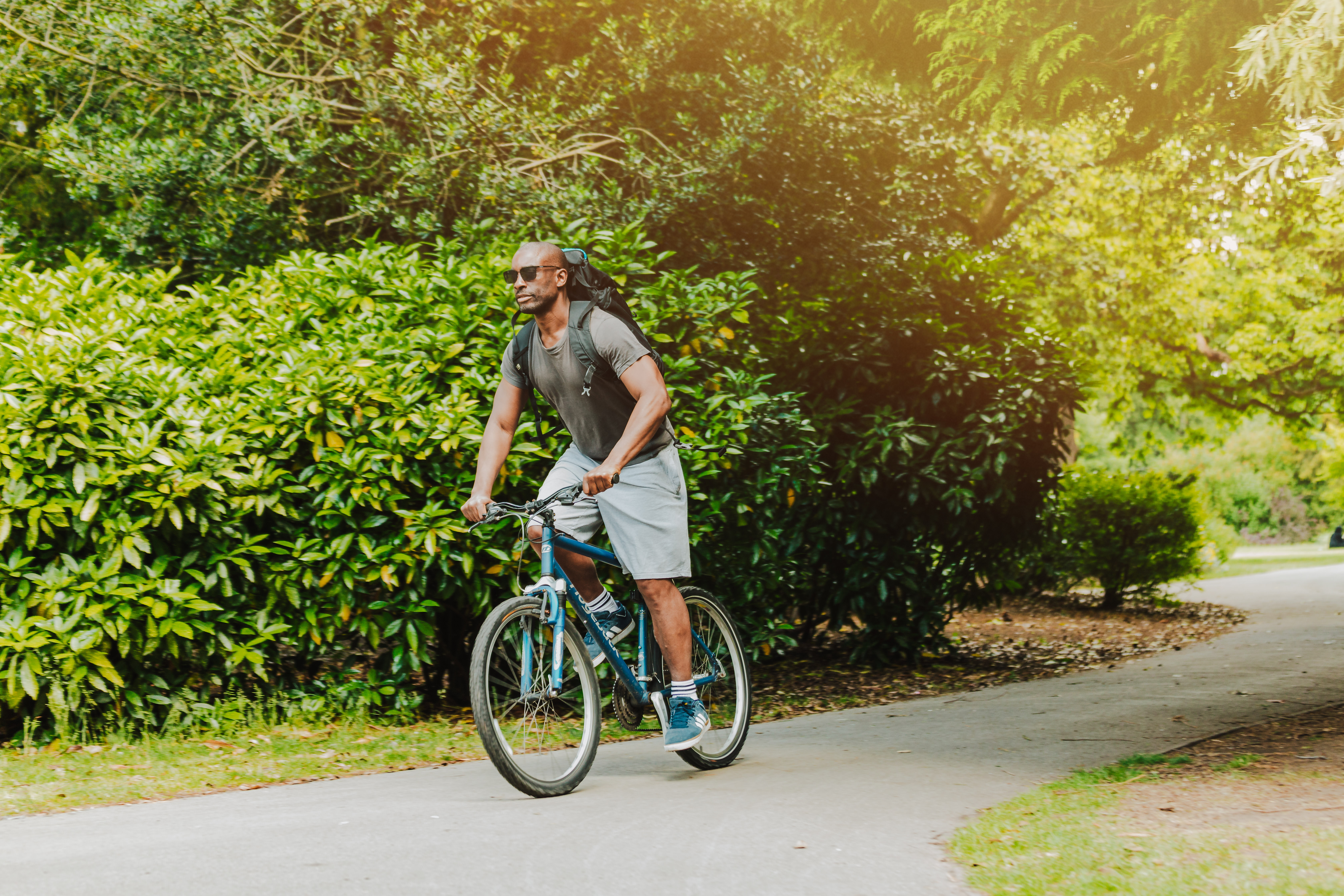 Man riding bike through park wearing sunglasses and a backpack
