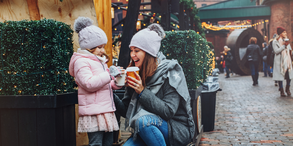 A mother and daughter enjoying hot drinks at a Christmas market.