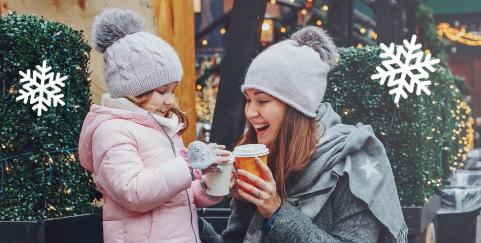 Two people in winter clothes holding hot drinks outdoors with festive decorations