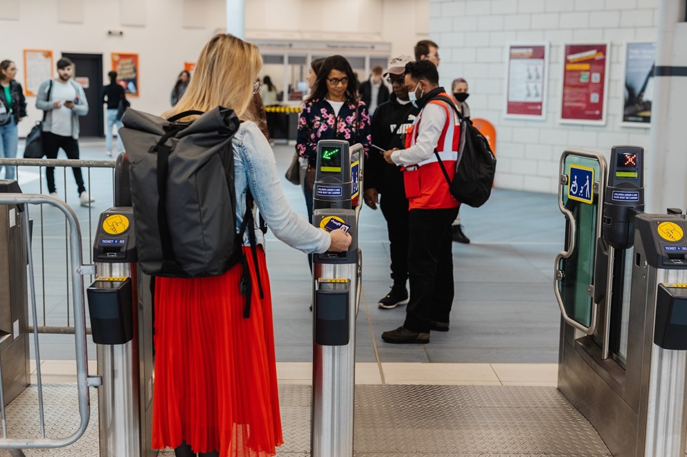 A woman scanning her ticket to exit the barriers at a train station. She is wearing a large work backpack.